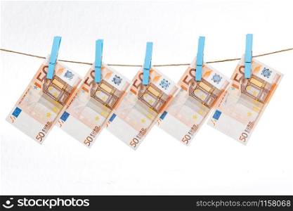 Euro banknotes are attached with blue clothespins to a rope on a white background