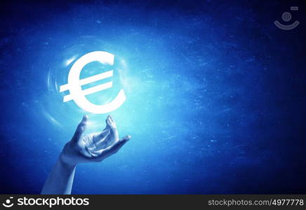 Euro currency. Close up of human hand holding euro symbol on blue background