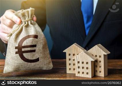 Euro money bags and residential buildings figures. Investments in real estate and construction industry. Taxes. Bank offer of mortgage loan. Rental business. Sale of housing. Buy. Municipal budget.
