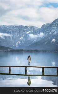 Europe travel locations image with a woman standing on a deck, admiring the view of the Austrian Alps mountains, reflected in the Hallstatter lake, Austria.