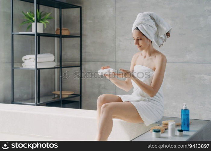 European beauty wraps in towel, applies body cream after bath. Woman showers, mornings at home. Anti-cellulite, massage, bodycare.