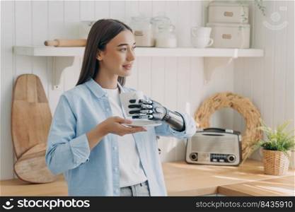 European disabled girl is holding cup with cyber hand. Woman has tea at domestic kitchen. Concept of grasp sensors in modern bionic prosthesis. Technologies and innovations for life quality.. European disabled girl is holding cup with cyber hand. Technologies for life quality.