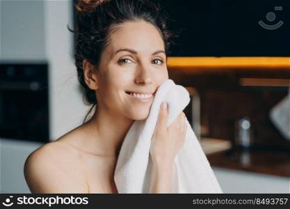 European girl is wiping face with towel after washing. Young brunette woman takes shower at home and doing skin care. Hygiene and freshness, dermatology and spa procedures.. European girl is wiping face with towel after washing. Young brunette woman takes shower at home.