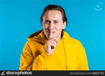 European handsome man holding finger on his lips over blue background. Gesture of shhh, secret, silence. High quality photo. European handsome man holding finger on his lips over blue background. Gesture of shhh, secret, silence