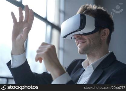 European man office employee wears formal suit and VR headset glasses excited of experiencing virtual reality stretching his hands up trying to catch seemingly round object totally immersed in 3D game. Europian man office employee wears formal suit and VRheadset excited of experiencing virtual reality
