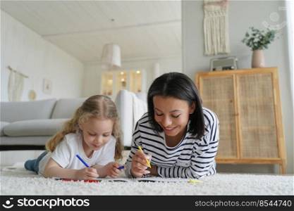 European mum and her kid are drawing together in living room. Carefree young woman and little girl lying on floor together and painting with colorful markers. Happy family enjoy time at home.. European mum and her kid are drawing together in living room. Happy family enjoy time at home.