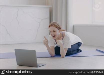 European white woman has distance sport classes. Girl gestures thumbs and feels good. Internet yoga lesson on mat. Concept of e-learning motivation. Sport online while coronavirus quarantine.. European white woman has distance sport classes. Girl gestures thumbs and feels good.