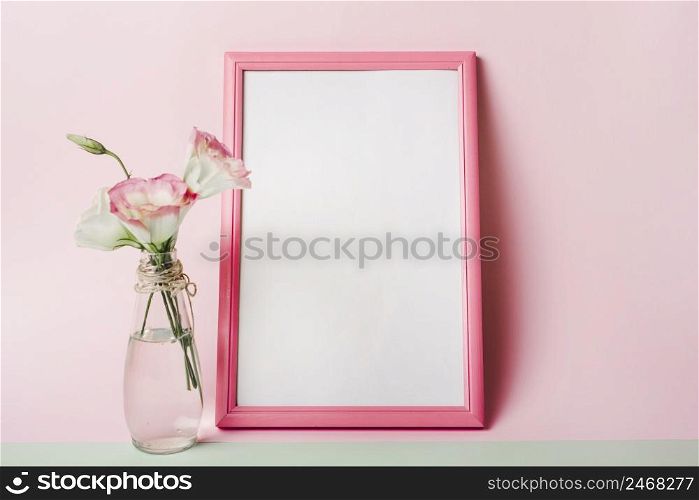 eustoma flowers vase near blank white frame with border against pink background