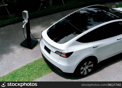 EV electric car charging in green sustainable city outdoor garden in summer. Urban sustainability lifestyle by green clean rechargeable energy of electric BEV vehicle innards. Young woman travel with EV electric car in green sustainable city innards