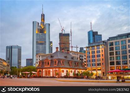 Evening Frankfurt cityscape, people walking by illuminated street with cafes and restaurants, modern architecture skyline at background, Frankfurt am Main, Germany