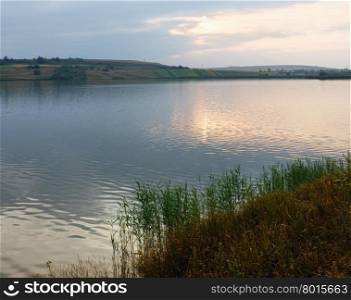 Evening lake scenery with sun reflection on water surface.