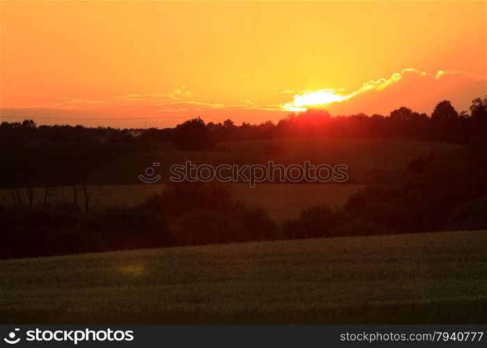Evening landscape. Beautiful sunset or sunrise over summer field meadow with dramatic red sky,