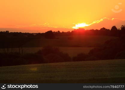 Evening landscape. Beautiful sunset or sunrise over summer field meadow with dramatic red sky,