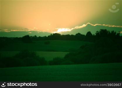 Evening landscape. Beautiful sunset or sunrise over summer green field meadow with dramatic red sky,