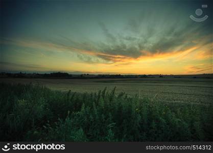 Evening landscape. Beautiful yellow sunset or sunrise over summer field meadow with dramatic red sky,