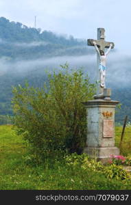 Evening mist over slope of summer mountain and crucifix of Jesus Christ(Carpathians, Lviv Oblast, Ukraine).