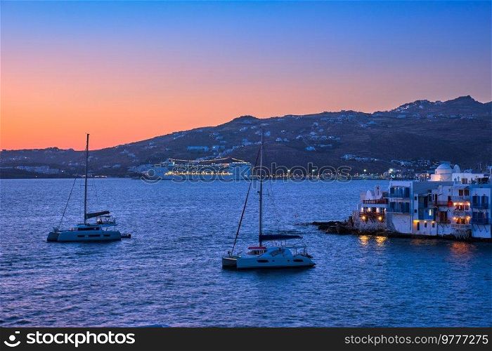 Evening on Mykonos island, Greece with yachts in the harbor and colorful waterfront houses of Little Venice romantic spot on sunset and cruise ship illuminated in night. Mykonos town, Greece. Sunset in Mykonos, Greece, with cruise ship and yachts in the harbor