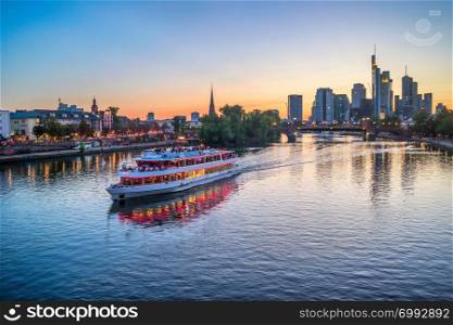 Evening over Main river with touristic cruise boat, illuminated embankment and Frankfurt skyline of modern architecture at sunset, Germany, Europe