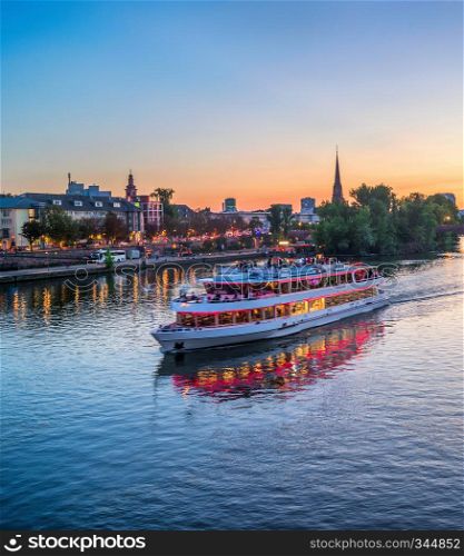 Evening over Main river with touristic cruise boat, illuminated embankment in Frankfurt Germany,