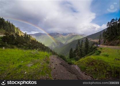 Evening rainbow in the gloomy sky above the mountain valley of Yading national level reserve, China