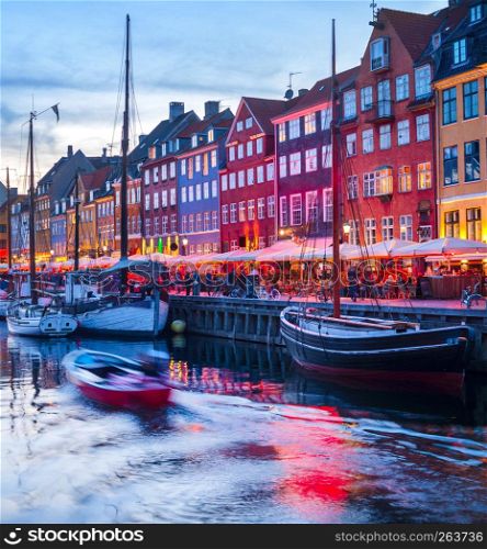 Evening scene with boats moored by illuminated Nyhavn harbor embankment, Copenhagen, Denmark