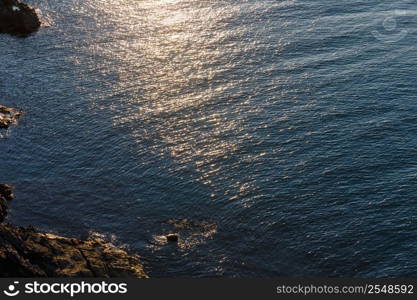 Evening sea rocky coast view with sun reflection on water surface.