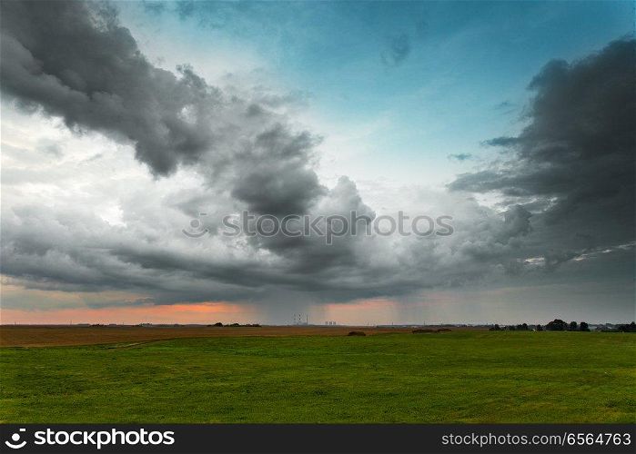 Evening storm. Dramatic clouds and sky over green fields and power plant