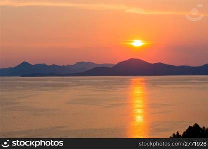 Evening summer coastline with pink-yellow sunset, sun track and Island on horizon. View from Peljesac peninsula (Croatia)