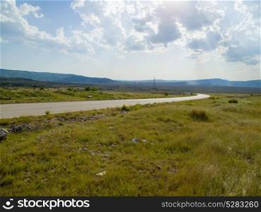 Evening summer landscape with green grass, road and clouds
