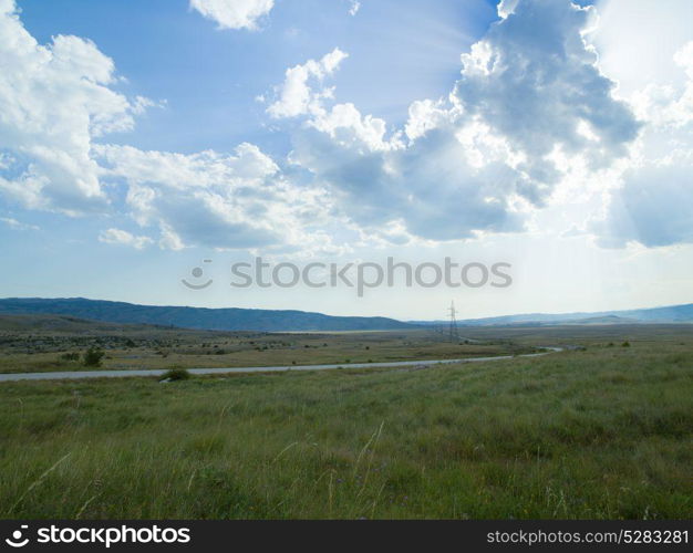 Evening summer landscape with green grass, road and clouds