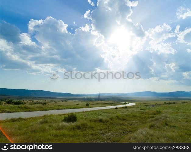 Evening summer landscape with green grass, road and clouds