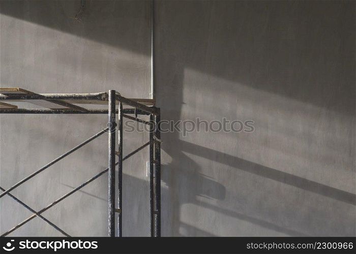 Evening sunlight and shadow on surface of scaffolding with electrical conduit pipe on loft cement wall in house construction site