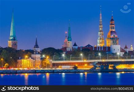 Evening view on the embankment of the Daugava River and the spiers of churches in Riga.. Riga. View the Church of St. Peter at night.