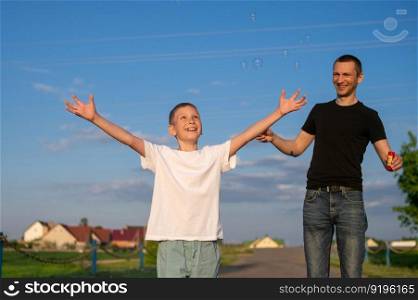 evening walk, white t-shirt, place for advertising, children’s things, dad and son, family weekend, soap bubbles, run, jump, stand, laugh. smile of a child, father, man, boy, child, adult. Dad blows soap bubbles emotional boy catches them