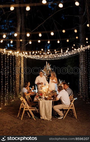 evening wedding family dinner in the forest with light bulbs and candles