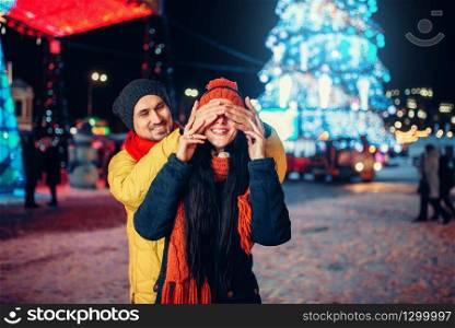 Evening winter walk, love couple plays guess who on the square. Man and woman having romantic meeting on city street with lights. Love couple plays guess who on the square