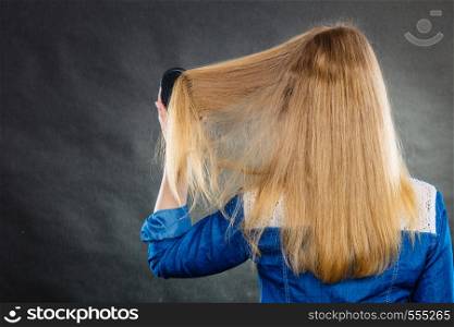 Everyday hygiene and care about good look. Back view of blonde casual girl combing her long straight hair. Woman using black comb hairbrush.. Blonde woman combing her hair.