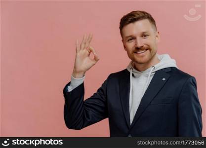 Everything is fine. Young joyful redhead man in casual wear showing ok sign and enjoying life, looking happily at camera while posing isolated over pink studio background. Body language concept. Cheerful man showing ok sign and smiling isolated over pink wall