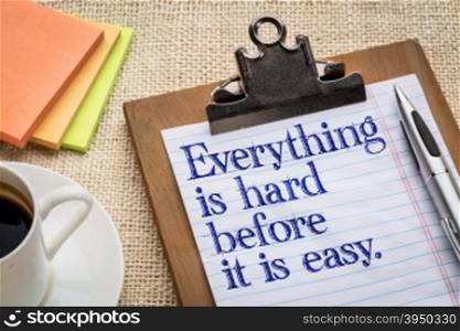 Everything is hard before it is easy - motivational slogan on a clipboard with a cup of coffee