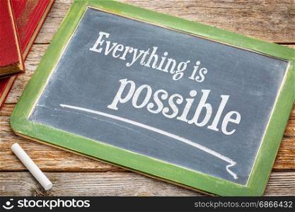 Everything is possible sign - a slate blackboard with a white chalk and a stack of books against rustic wooden table