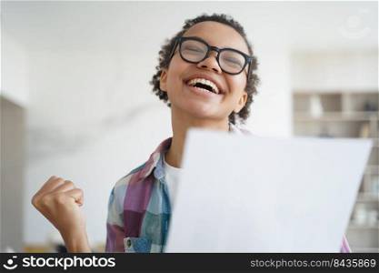 Exam is passed successfully. Overjoyed african american girl holding letter from university. Teenage girl is accepted to college and celebrating her victory. Goal achievement and victory concept.. Overjoyed african american girl holds letter from university. Goal achievement and victory concept.