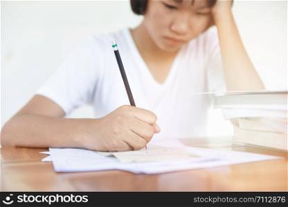 exam stress / education young female college in class taking notes and using a pencil sitting learning concept stressed student girl asian take the exam final with books on the table