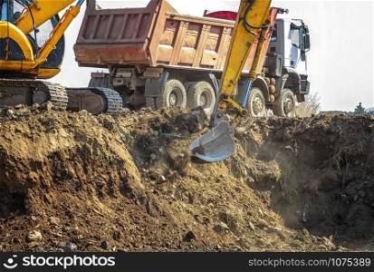 Excavator is loading excavation on the truck. Heavy construction equipment consisting of a boom, dipper or stick, bucket, and cab on a rotating platform.
