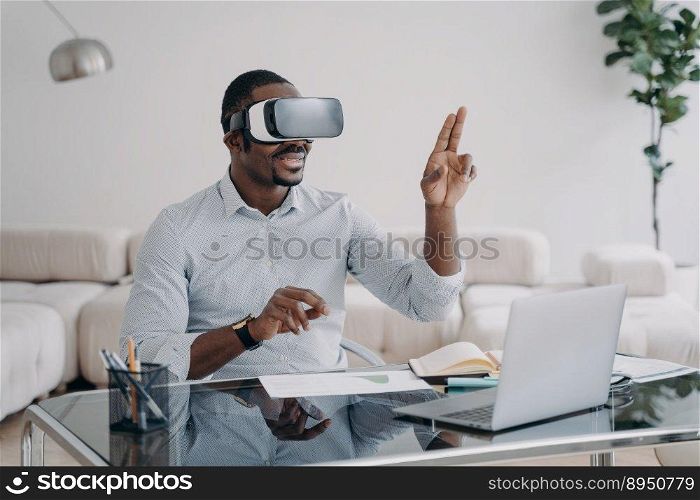 Excited afro man in vr glasses at workplace at home. Businessman has virtual meeting. Freelancer is working on design project. Modern wireless technology for remote work and entertainment.. Excited afro man in vr glasses at workplace at home. Businessman has virtual meeting.