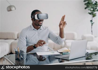 Excited afro man in vr glasses at workplace at home. Businessman has virtual meeting. Freelancer is working on design project. Modern wireless technology for remote work and entertainment.. Excited afro man in vr glasses at workplace at home. Businessman has virtual meeting.