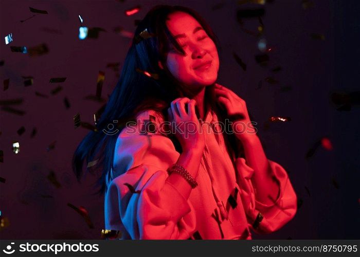 Excited asian attractive woman dancing, having fun, rejoices over confetti rain with neon light in studio. Concept of happiness, party, winning.. Excited asian attractive woman dancing, having fun, rejoices over confetti rain with neon light in studio. Concept of happiness, party, winning