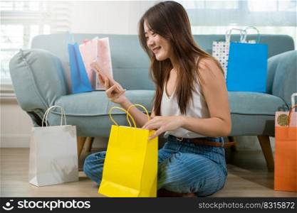 Excited Asian buying woman holding mobile phone with many shopping bags at home in living room shopping, Happy female online shopping payment sitting on couch with smartphone, Black Friday