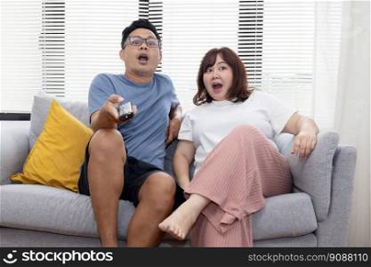 Excited Asian Couple with TV Remote  Control Watching Television on the Couch