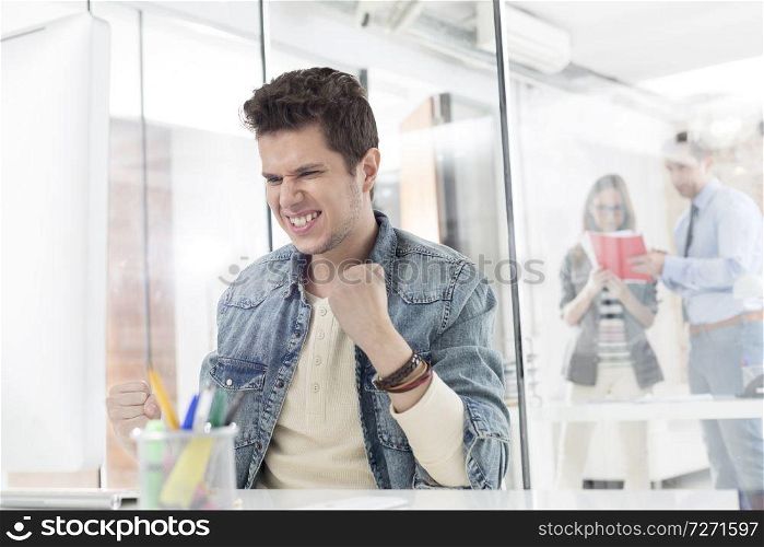 Excited businessman celebrating success at computer desk in office