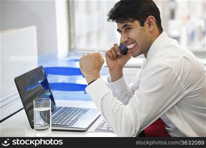 Excited businessman using cell phone at office desk